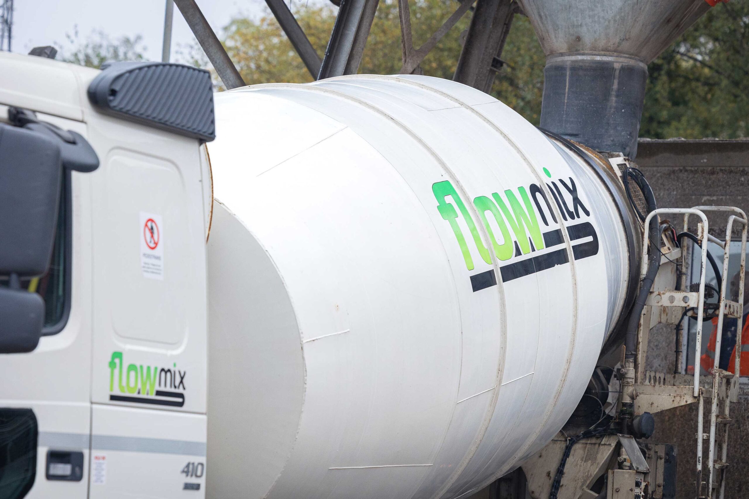 Close-up of a white Flowmix concrete mixer truck with the Flowmix logo on the drum at a batching site.